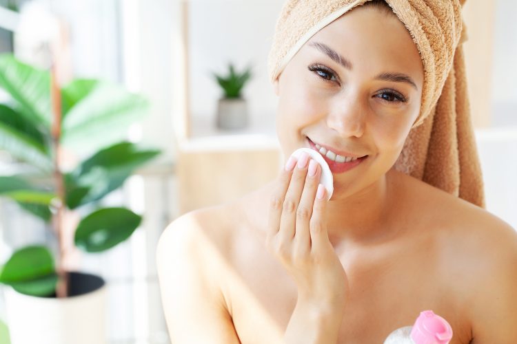 Woman using applying cream softening moisturizer with cotton pad on her face, removing cosmetics.